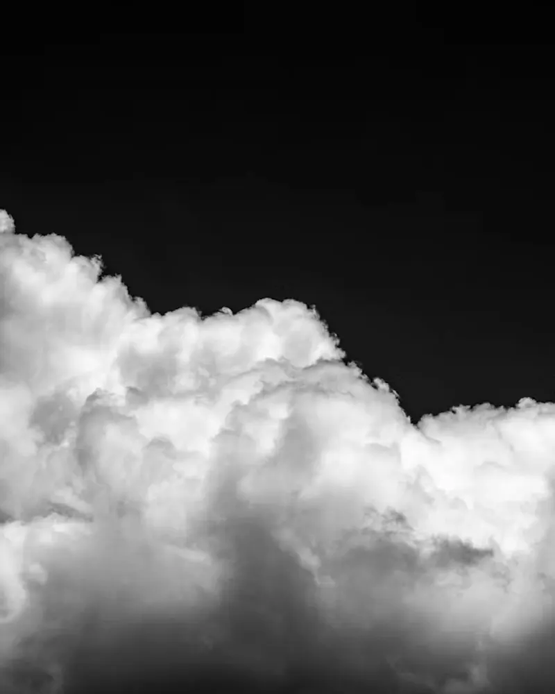 Nuvens volumosas iluminadas contra céu escuro, em preto e branco